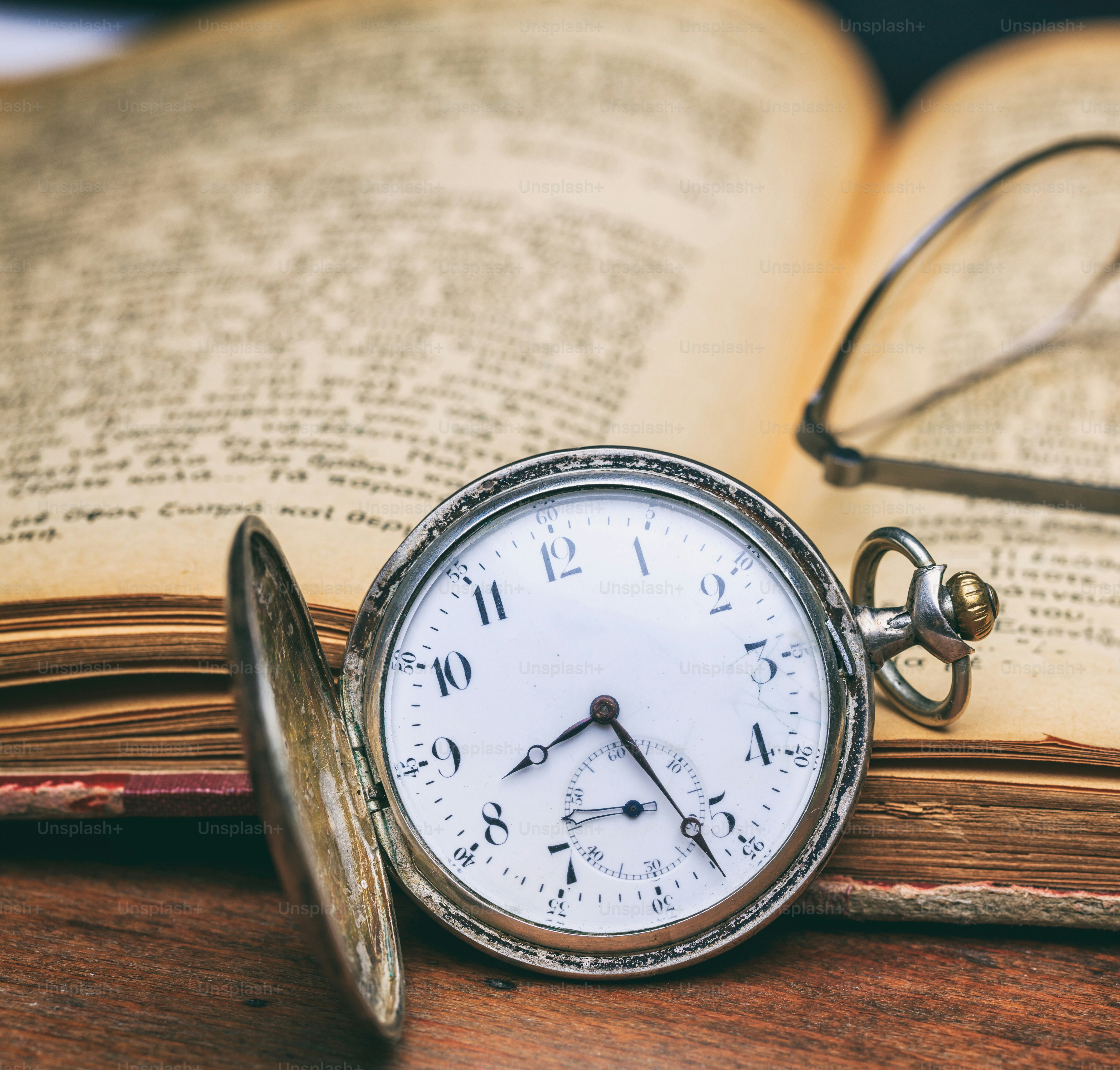 Vintage pocket watch and open old book on a wooden office desk background, closeup view. Time, science concept
